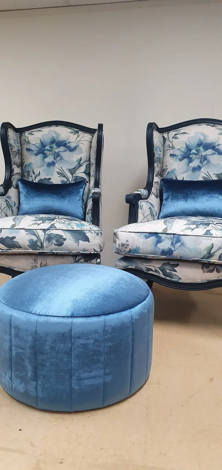 Pair of wingback armchairs reupholstered in blue floral fabric with a blue velvet ottoman